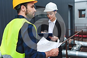 selective focus of architect and builder in helmets with blueprint and clipboard