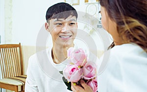 Selective focus Asian handsome man show the love and give flowers or pink roses to his girlfriend in bedroom on valentine`s day.