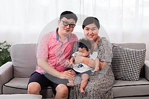 Selective focus Asian happy family sitting on cozy sofa cuddling with adorable infant take a photo in living room. Newborn baby