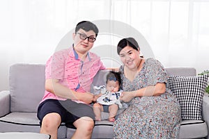 Selective focus Asian happy family sitting on cozy sofa cuddling with adorable infant take a photo in living room. Newborn baby