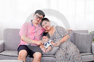 Selective focus Asian happy family sitting on cozy sofa cuddling with adorable infant take a photo in living room. Newborn baby