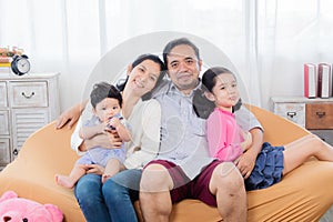 Selective focus Asian happy family sitting on cozy sofa cuddling with two little children take a photo in living room. Sibling