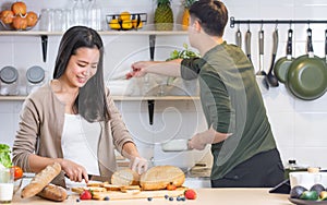 Selective focus Asian happy young adult woman cooking in cozy home kitchen in morning, preparing meal, making salad, bread for