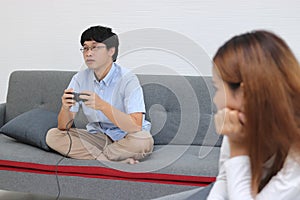 Selective focus on Asian man playing game with unhappy angry woman after arguing in living room. Bad relationship couple concept