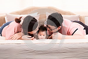 Selective focus of asian newborn baby lying down on bed with mother and father, happy mom and dad kiss the head adorable infant