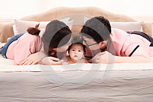 Selective focus of asian newborn baby lying down on bed with mother and father, happy mom and dad kiss the head adorable infant