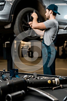 selective focus of auto mechanic in uniform fixing car wheel