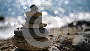 Selective focus. Balanced stone pyramid of pebbles on a background of blue sea, sunny bokeh path. Zen stones on sea
