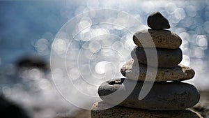 Selective focus. Balanced stone pyramid of pebbles on a background of blue sea, sunny bokeh path. Zen stones on sea