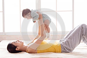 Selective focus Beautiful Asian mother lying on bed and holding infant in air, mom looking baby with love and tender while playing