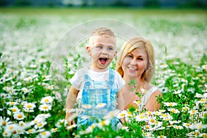 Selective focus. A blond son and mother in a field of daisies in bloom. Enjoy the fragrance of a bouquet of chamomile