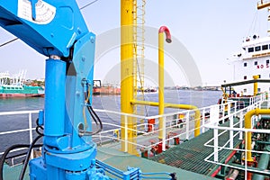 Selective focus at blue crane machine on steel walkway over gas pipelines system in oil tanker ship at harbor, perspective side