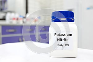 Selective focus of a bottle of potassium nitrite preservative chemical compound. White laboratory background with copy space.