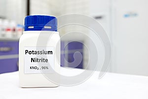 Selective focus of a bottle of potassium nitrite preservative chemical compound. White laboratory background with copy space.