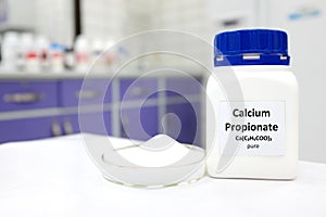 Selective focus of bottle of pure calcium propionate food additive beside a petri dish with white solid powder substance.