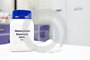 Selective focus of bottle of pure monosodium glutamate or msg food additive beside a petri dish with white solid powder substance.