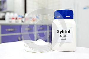 Selective focus of a bottle of pure xylitol sugar substitute with powder in petri dish. White laboratory background
