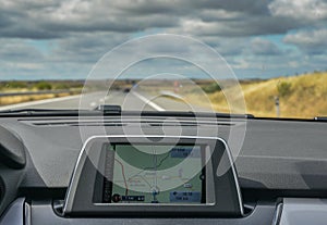 Selective focus of built in GPS navigator on dashboard of a car going down the scenic highway in Algarve, Portugal