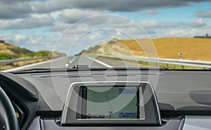 Selective focus of built in GPS navigator on dashboard of a car going down the scenic highway in Algarve, Portugal