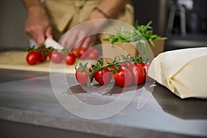 Selective focus on a bunch of red ripe tomato cherry on the kitchen table against the background of a male chef chopping
