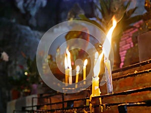 Selective focus of burning candles on a shelf with a burry background of a Buddha statue sitting in a deep cave