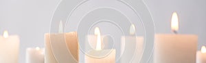 Selective focus of burning white candles glowing isolated on grey, panoramic shot