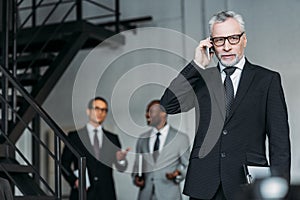 selective focus of businessman talking on smartphone with colleagues behind