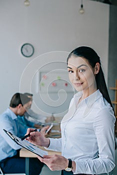 selective focus of businesswoman with notepad and colleagues at workplace