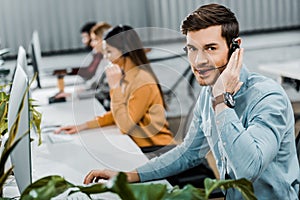 Selective focus of call center operator looking at camera while multiethnic colleagues working