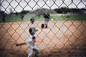 Selective focus on chain link fence with a youth baseball game defocused and blurred in the background