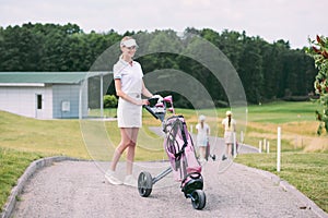 selective focus of cheerful female golf player in cap and white polo with golf gear