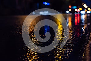 Selective focus of city road and car during rain at night, with unfocused lights from headlights of cars. Water from rain and