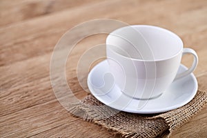 Selective focus close-up picture of empty white teacup and saucer on rustic vintage background with homespun napkin