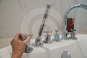 selective focus close up woman hand turn to adjust hot and cold water of bathtub faucet in luxury hotel bathroom