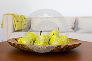 Selective focus closeup of Bartlett pears in golden plate on walnut coffee table, with beige couch