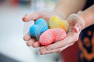 Selective focus colorful multicolor knitting hearts held by female`s both hands, representing helping hands, supports, assistance,