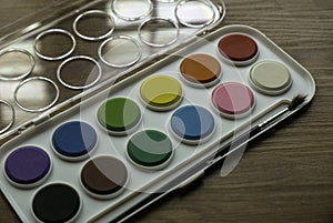 Selective focus of colorful watercolor palette with brush on wooden background