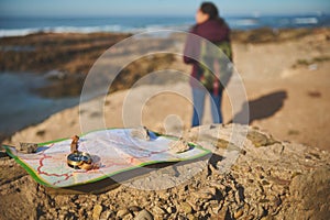 Selective focus on compass and map on the rock over blurred background of a backpack female tourist enjoying his journey