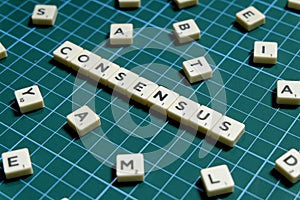 Selective focus of Consensus word made of square letter block on green square mat background