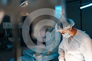 Selective focus of cooperating team of surgeons processing surgical operation in dark operating room modern hospital