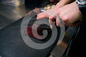 Selective focus of cropped male chef cutting meat with knife on chopping board