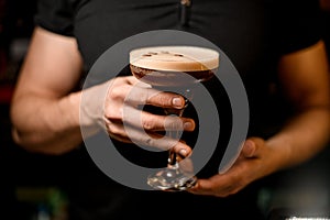 Selective focus on crystal glass with tasty foamy alcoholic cocktail decorated with coffee beans in male hands.