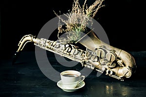 Selective focus on cup of coffee with vintage saxophone and dry field flowers