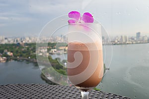 Selective focus on cup of juice fruit against aerial scene of cityscape with lake. Concept of leisure time having drink outdoor, o