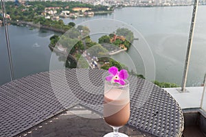 Selective focus on cup of juice fruit against aerial scene of cityscape with lake. Concept of leisure time having drink outdoor, o