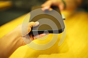 Selective focus customer hand receive bill payment receipt in black leather folder holder tray on yellow wooden table background