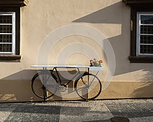 selective focus on cute old bicycle table with flowers on the street between wooden windows on the wall