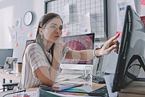 Selective focus of data analyst pointing with finger at computer monitor near papers and glass of water