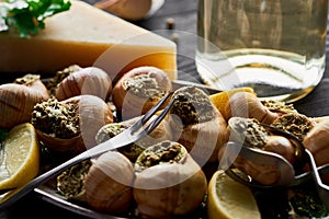 Selective focus of delicious cooked escargots with lemon, parmesan, cutlery, parsley and white wine on black wooden