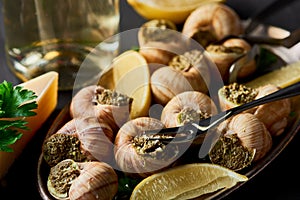 Selective focus of delicious cooked escargots with lemon, parmesan, cutlery, parsley and white wine on black wooden